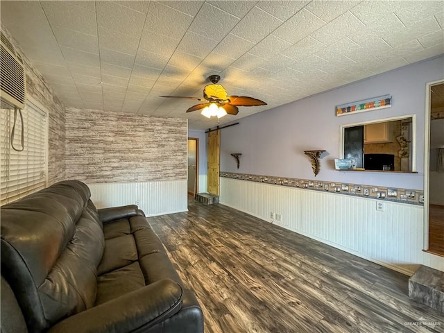 unfurnished living room featuring ceiling fan, a barn door, and dark wood-type flooring