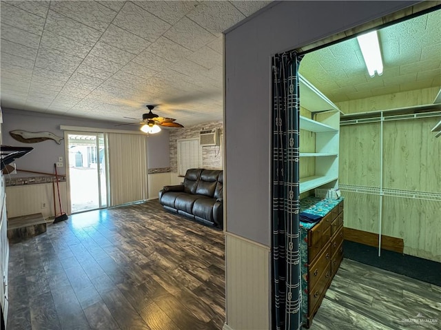 interior space with ceiling fan, wooden walls, a wall mounted air conditioner, and dark hardwood / wood-style floors