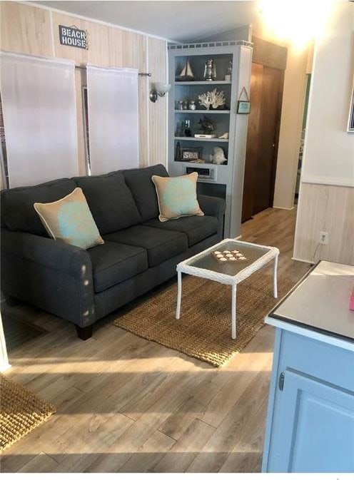 living room with built in shelves, wood walls, and light hardwood / wood-style flooring