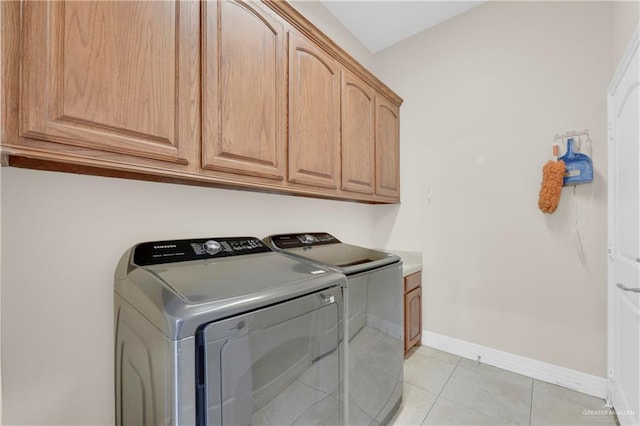 clothes washing area with cabinets, light tile patterned flooring, and washing machine and clothes dryer