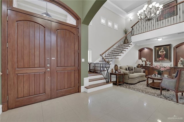 entryway with a notable chandelier, light tile patterned flooring, ornamental molding, and a high ceiling