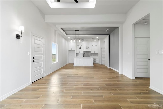 unfurnished living room with light wood-style floors, a sink, and baseboards