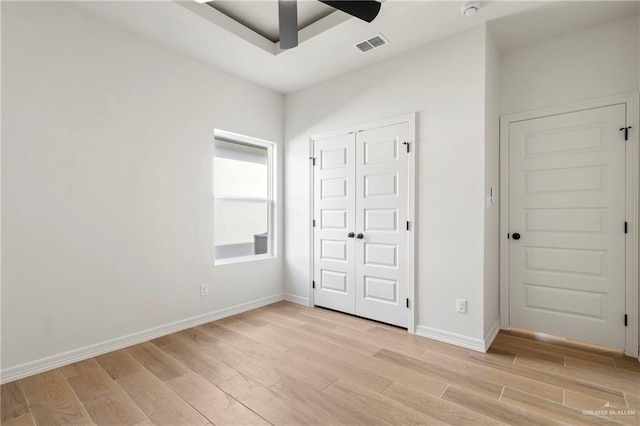 unfurnished bedroom featuring a ceiling fan, visible vents, baseboards, a closet, and light wood-style flooring
