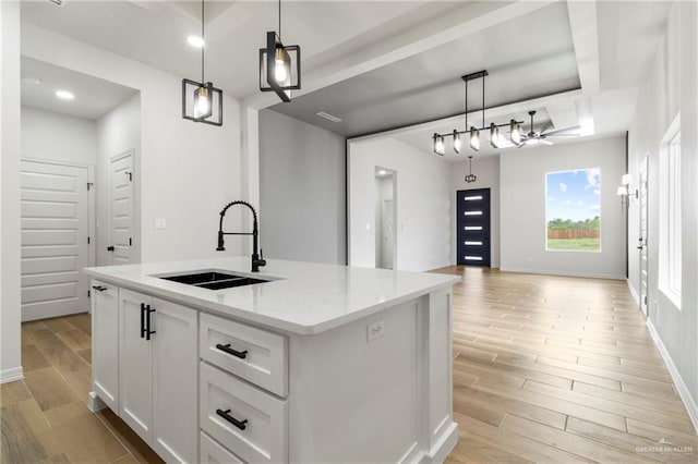 kitchen featuring open floor plan, a center island with sink, a sink, and light wood-style floors