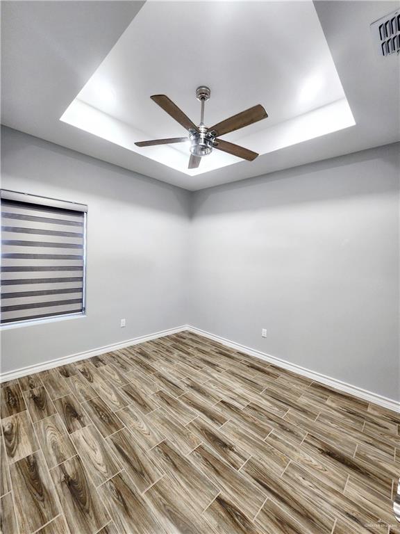 spare room featuring a raised ceiling, ceiling fan, and wood-type flooring