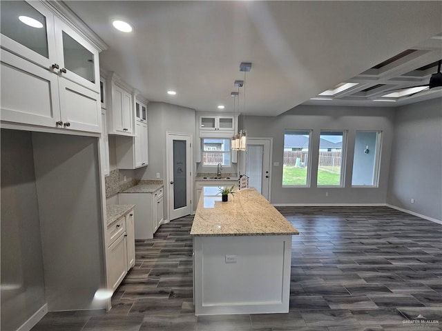 kitchen with a kitchen island with sink, white cabinets, light stone countertops, and dark hardwood / wood-style floors