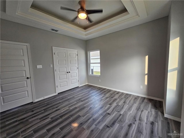 unfurnished bedroom featuring a raised ceiling, ceiling fan, and dark hardwood / wood-style floors