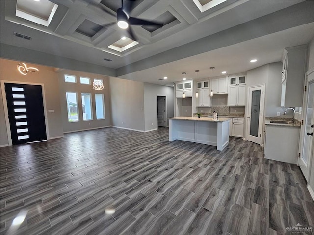 kitchen featuring coffered ceiling, dark wood-type flooring, sink, a center island with sink, and white cabinets