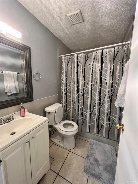 1414 Vatia Blvd, Mission, TX 78572 - bathroom featuring vanity, a textured ceiling, tile walls, tile patterned floors, and curtained shower