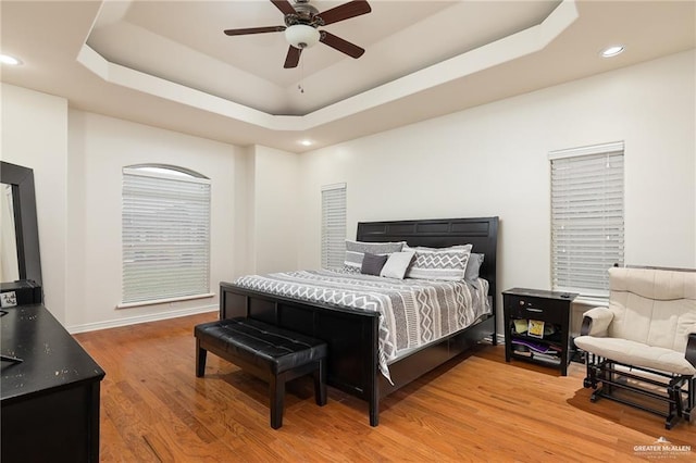 bedroom featuring hardwood / wood-style floors, a raised ceiling, and ceiling fan