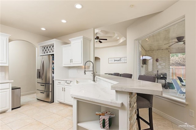 kitchen with sink, stainless steel fridge with ice dispenser, kitchen peninsula, a breakfast bar area, and white cabinets