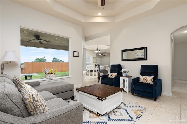 living room featuring ceiling fan with notable chandelier, light tile patterned flooring, and a raised ceiling