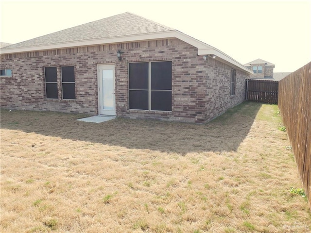 back of house featuring brick siding, a lawn, a shingled roof, and a fenced backyard