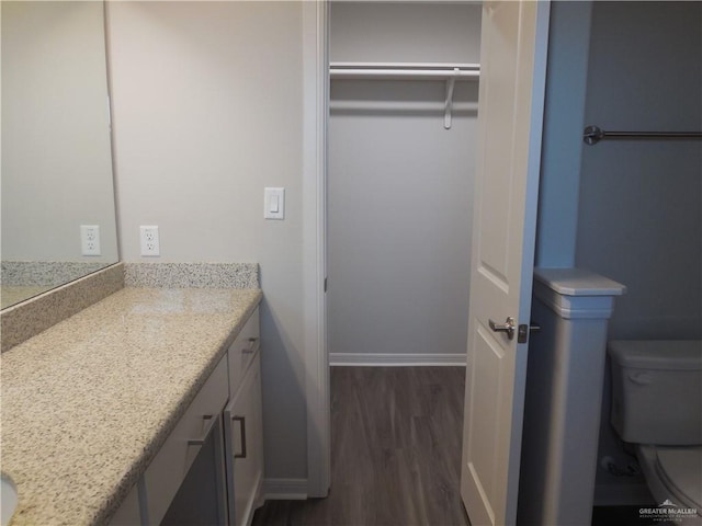 bathroom featuring toilet, wood finished floors, vanity, baseboards, and a spacious closet