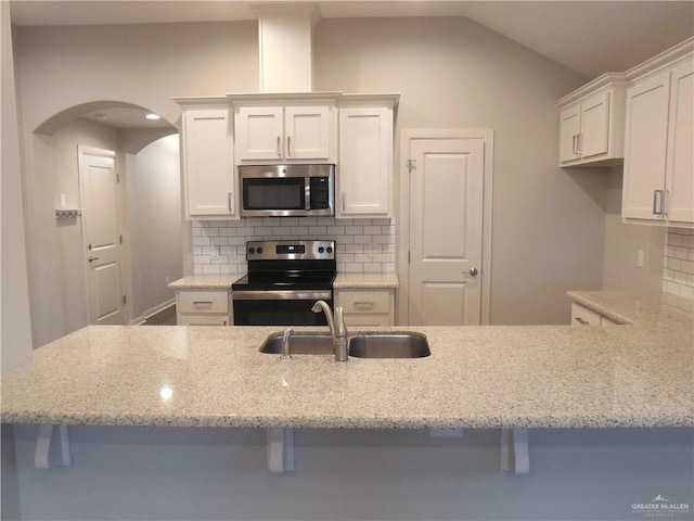 kitchen with backsplash, light stone counters, appliances with stainless steel finishes, white cabinetry, and a sink