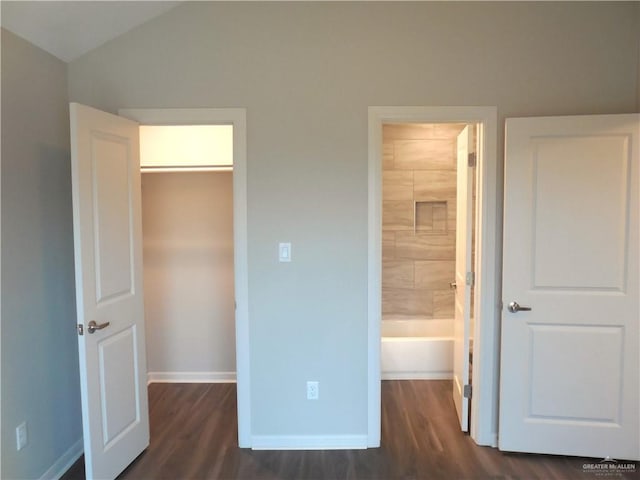 unfurnished bedroom with dark wood-style floors, lofted ceiling, a walk in closet, and baseboards