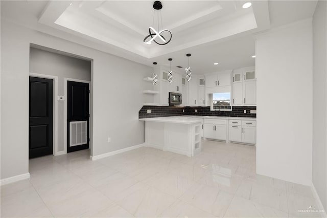 kitchen featuring kitchen peninsula, a raised ceiling, decorative light fixtures, and white cabinetry