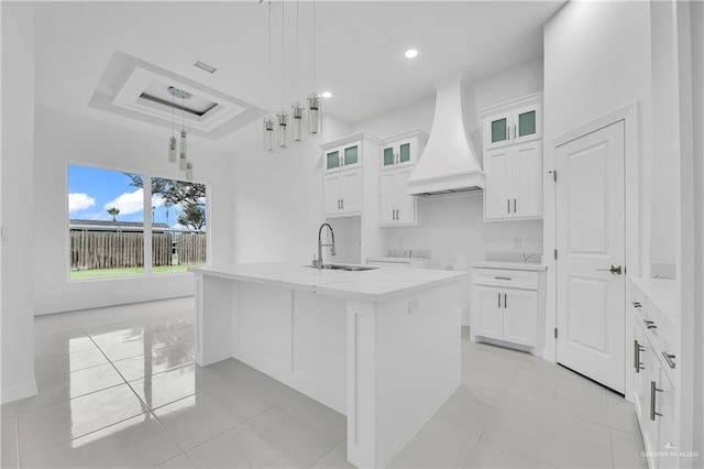 kitchen with white cabinets, custom exhaust hood, decorative light fixtures, and a kitchen island with sink