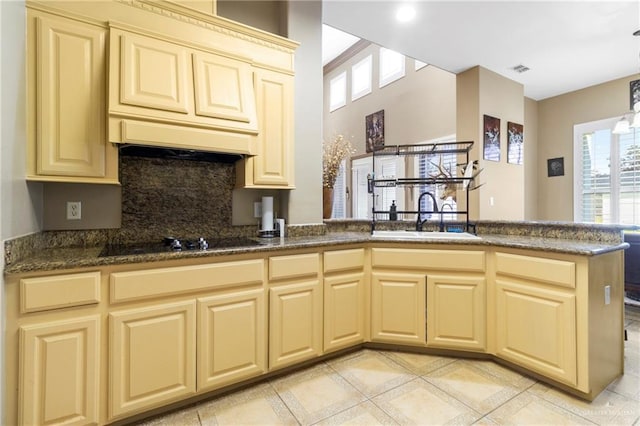 kitchen with tasteful backsplash, dark stone countertops, a peninsula, black electric cooktop, and a sink