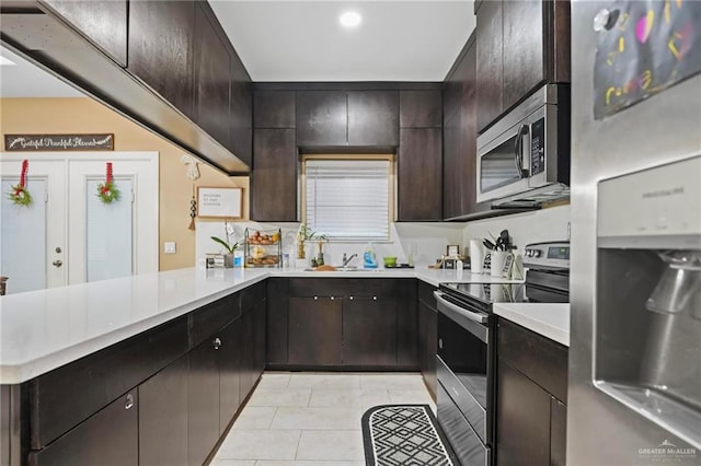 kitchen featuring kitchen peninsula, appliances with stainless steel finishes, dark brown cabinetry, and light tile patterned floors