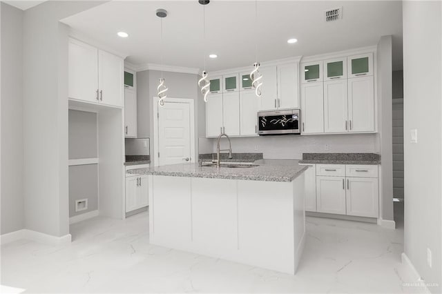 kitchen with sink, hanging light fixtures, an island with sink, light stone counters, and white cabinetry