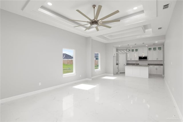 unfurnished living room featuring a raised ceiling, ceiling fan, and sink