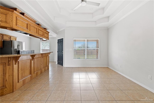 kitchen featuring stainless steel fridge, light tile patterned floors, a raised ceiling, and crown molding