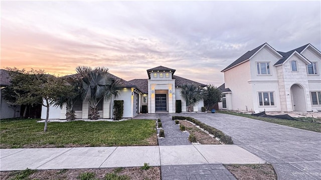 view of front of property featuring decorative driveway, a yard, and stucco siding