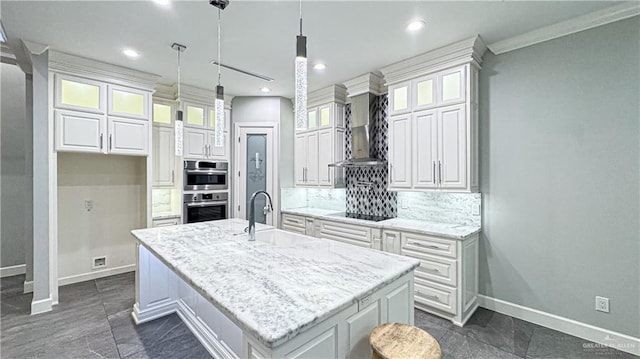 kitchen featuring black electric stovetop, backsplash, white cabinets, a sink, and wall chimney range hood