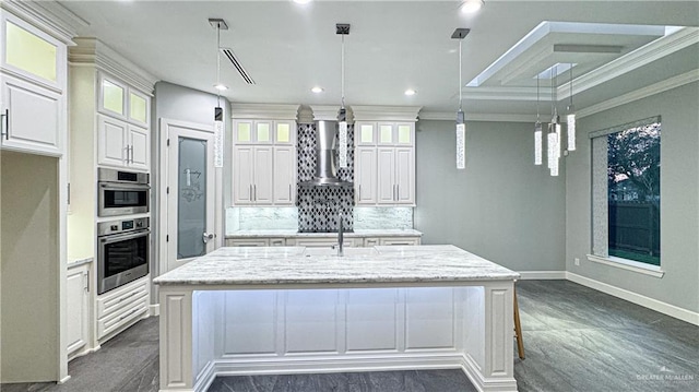 kitchen featuring crown molding, a center island with sink, decorative backsplash, white cabinetry, and wall chimney range hood