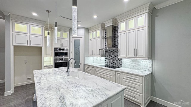 kitchen with tasteful backsplash, wall chimney exhaust hood, black electric cooktop, white cabinetry, and a sink