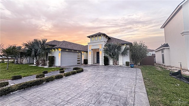 view of front facade with a garage, decorative driveway, a lawn, and stucco siding