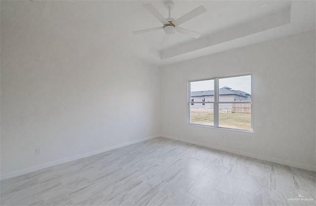 empty room with ceiling fan and a tray ceiling