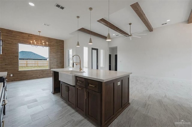 kitchen with sink, hanging light fixtures, wooden walls, a kitchen island with sink, and ceiling fan with notable chandelier