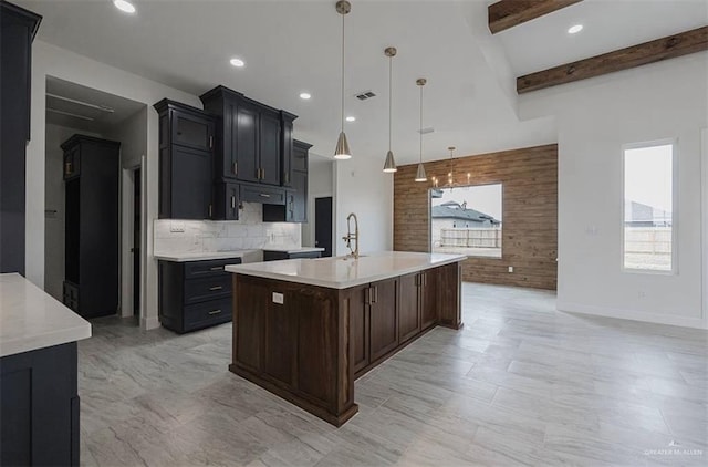 kitchen with a center island with sink, hanging light fixtures, wooden walls, decorative backsplash, and beam ceiling