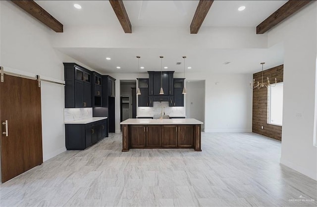 kitchen featuring pendant lighting, a barn door, an island with sink, and beamed ceiling