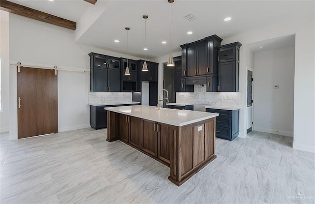 kitchen with decorative backsplash, a barn door, an island with sink, decorative light fixtures, and beam ceiling