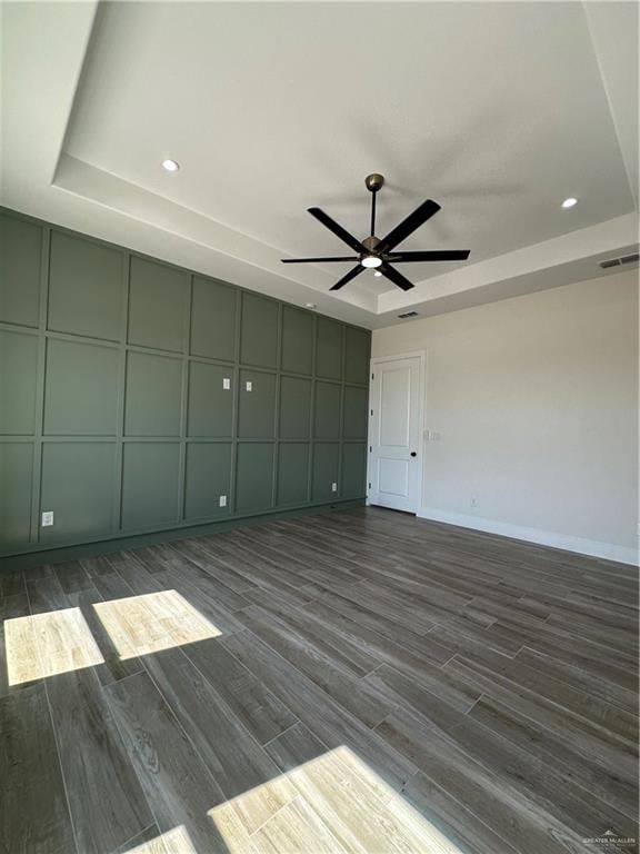 empty room featuring a raised ceiling, ceiling fan, and dark hardwood / wood-style floors