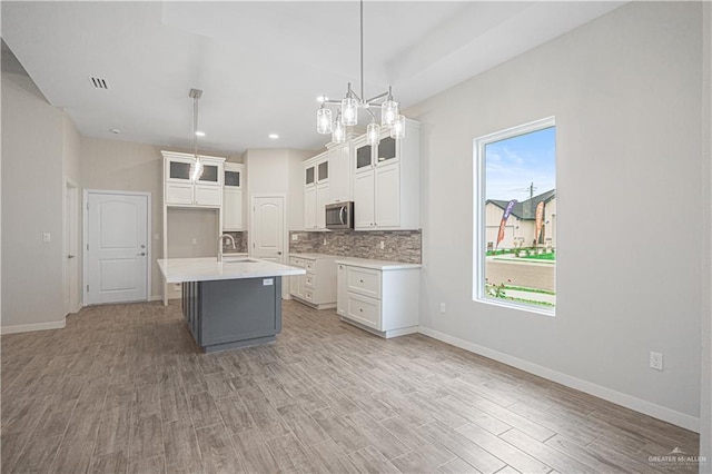 kitchen with backsplash, a kitchen island with sink, light hardwood / wood-style floors, white cabinetry, and hanging light fixtures