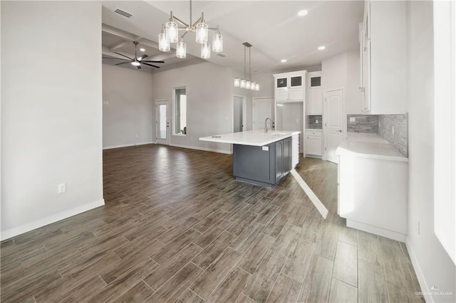 kitchen featuring ceiling fan, dark wood-type flooring, pendant lighting, white cabinets, and an island with sink