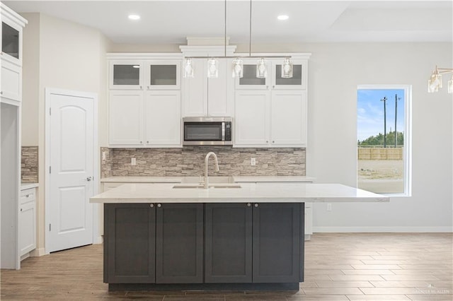 kitchen with pendant lighting, a kitchen island with sink, white cabinets, sink, and light wood-type flooring