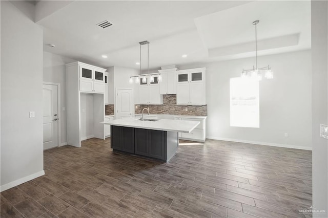 kitchen with tasteful backsplash, white cabinets, dark hardwood / wood-style floors, hanging light fixtures, and an island with sink