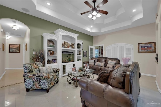 living room featuring a ceiling fan, a tray ceiling, baseboards, tile patterned flooring, and recessed lighting