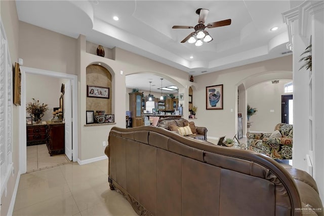living area featuring recessed lighting, a raised ceiling, a ceiling fan, arched walkways, and baseboards