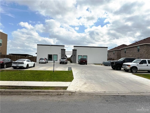 view of front of home with uncovered parking, a front yard, fence, and stucco siding