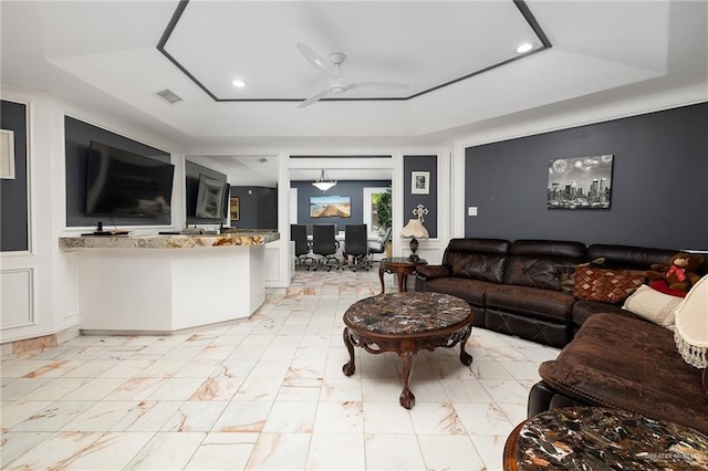living area with a ceiling fan, a tray ceiling, recessed lighting, and marble finish floor