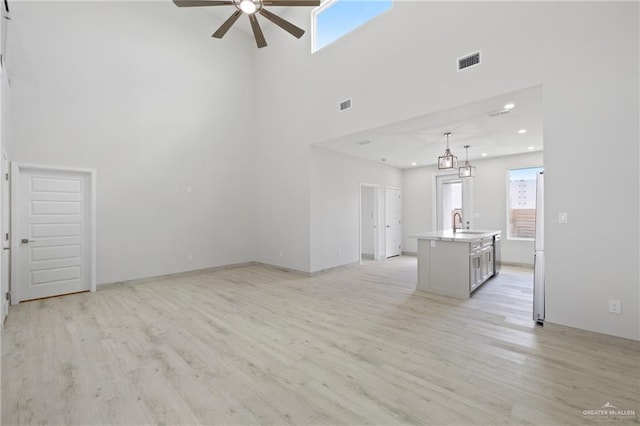 1220 N Lincoln Ave, San Juan, TX 78589 - unfurnished living room featuring a ceiling fan, a towering ceiling, light wood finished floors, plenty of natural light, and a sink