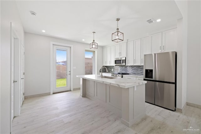 1220 N Lincoln Ave, San Juan, TX 78589 - kitchen with stainless steel appliances, a sink, light wood-style flooring, white cabinetry, and a center island with sink