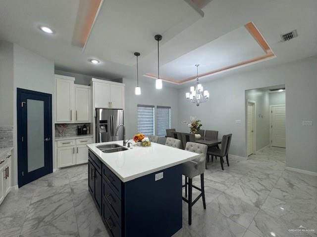 kitchen featuring white cabinets, pendant lighting, stainless steel fridge, and a kitchen island with sink