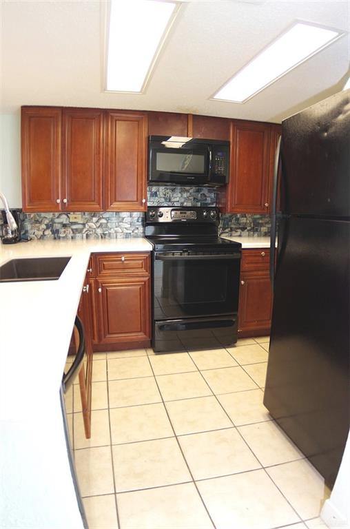 kitchen featuring light tile patterned flooring, sink, backsplash, and black appliances